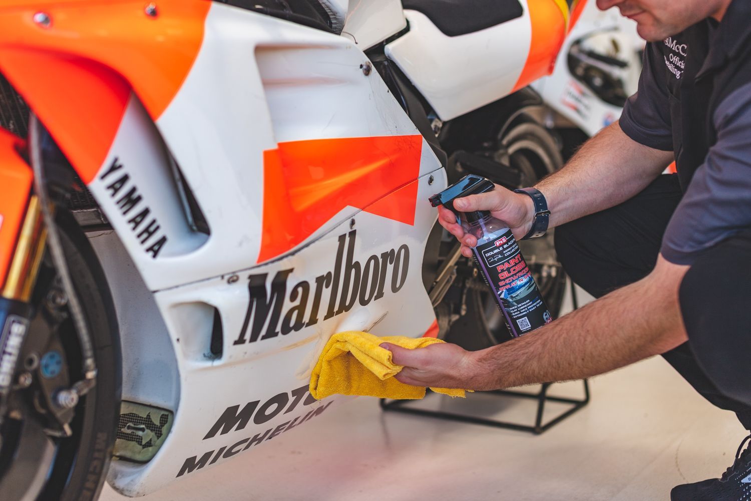 Man cleans a white and orange Yamaha motorcycle with a Marlboro logo in an indoor setting.