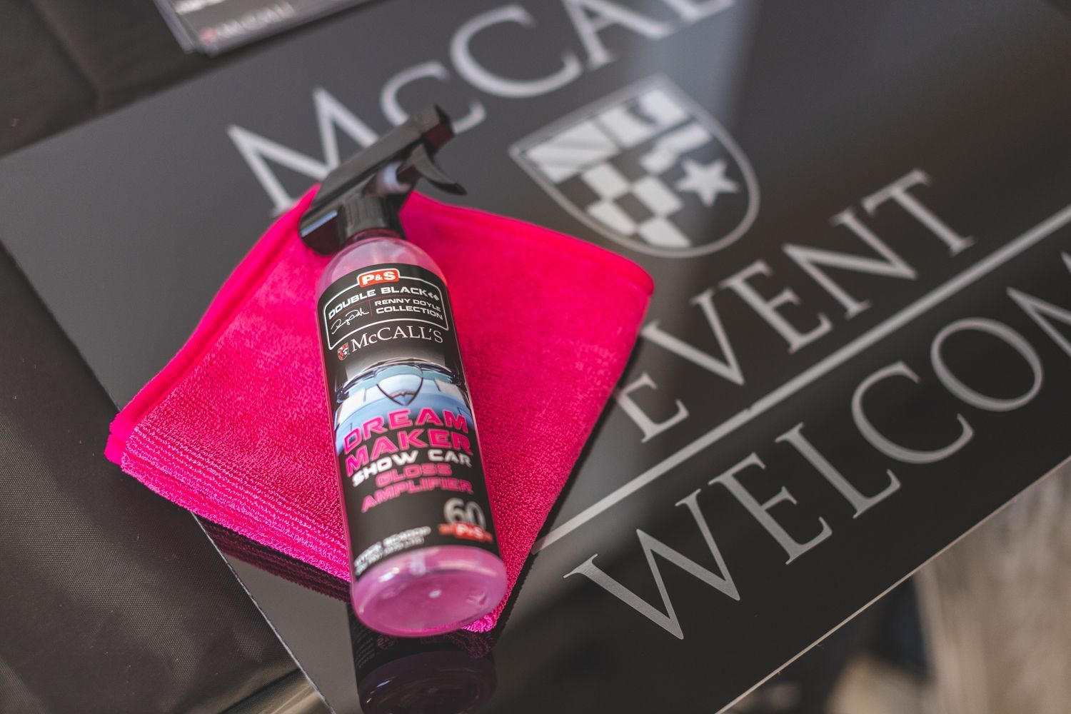 Pink car detailing spray and microfiber cloth on a black welcome sign.
