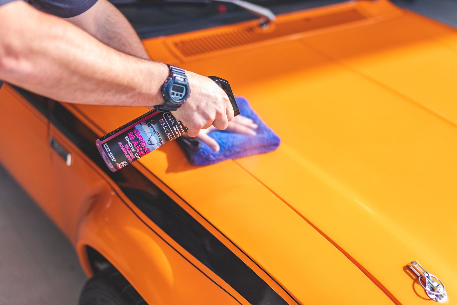 Person spraying detailer on an orange car and wiping with a blue cloth.