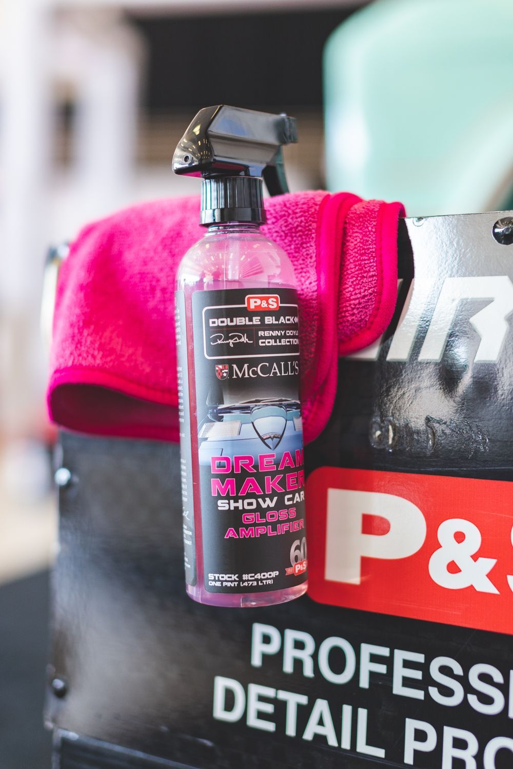 Pink car detailing spray bottle with a pink cloth on a black toolbox.