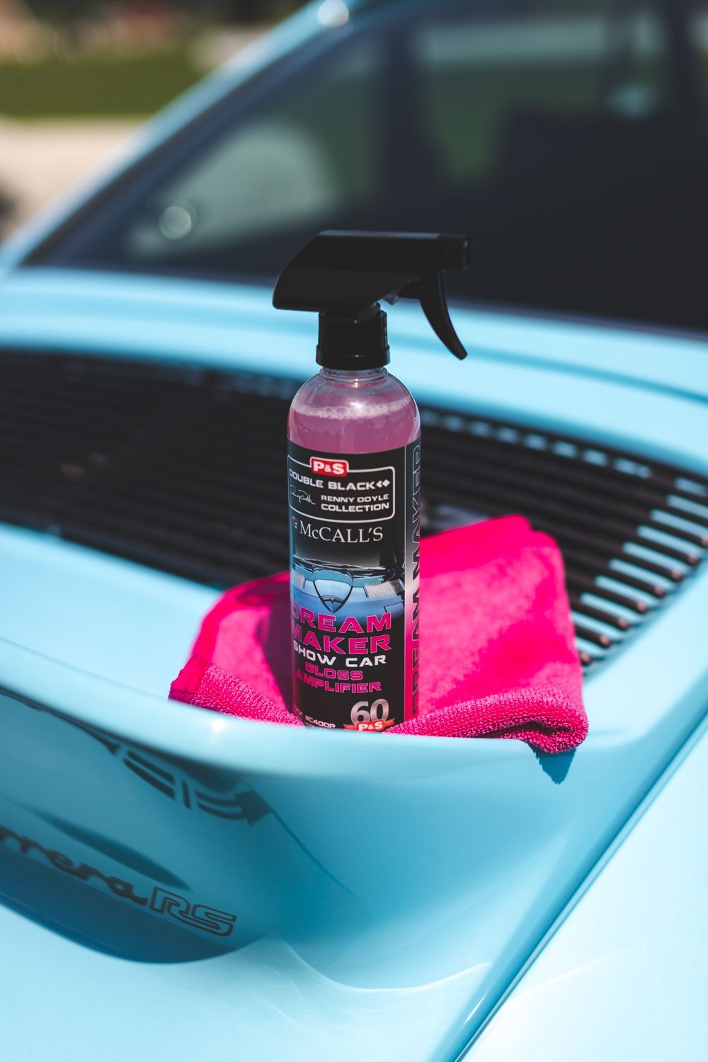 Spray bottle and pink microfiber towel on a light blue Porsche hood.