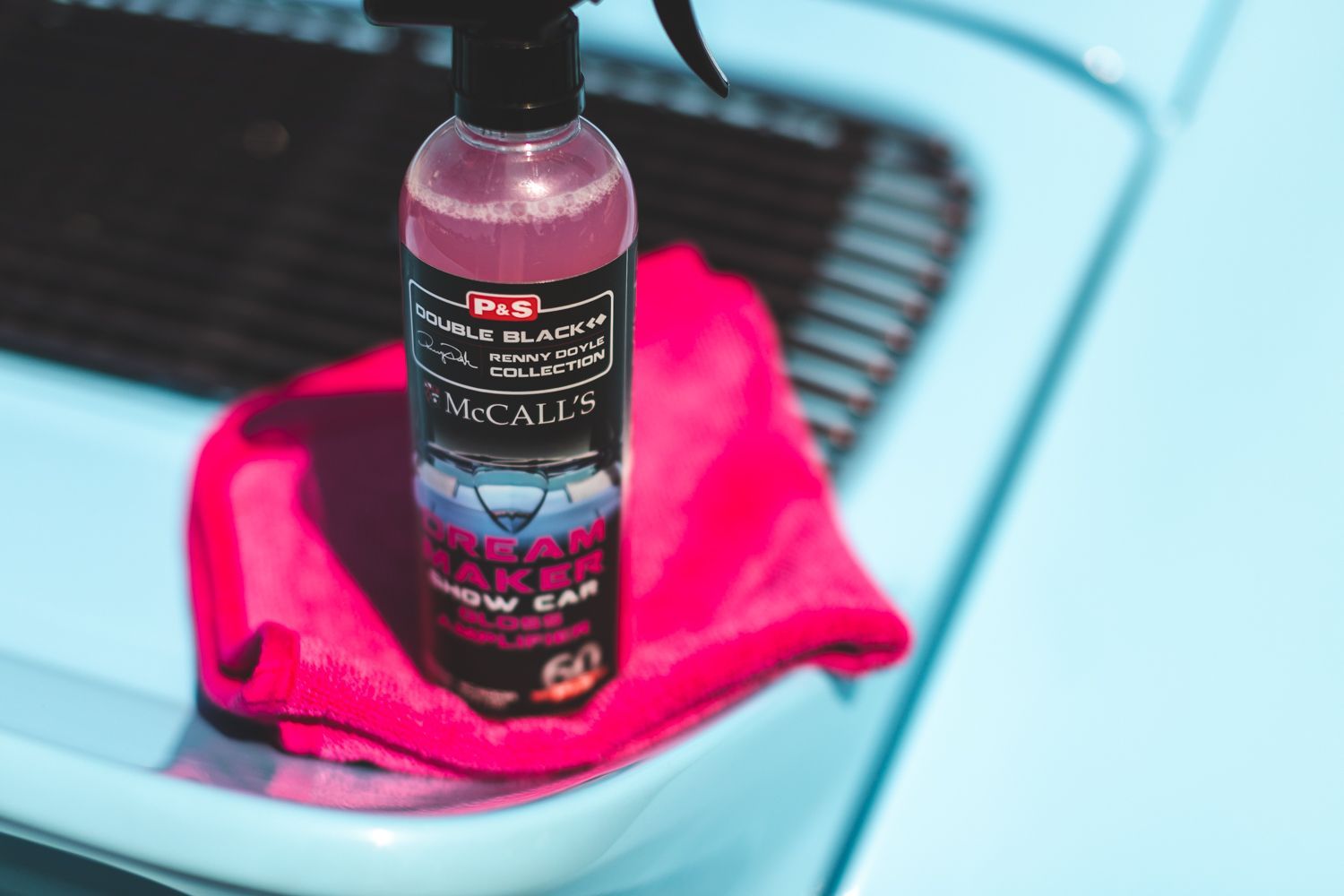 A spray bottle and pink cloth on a light blue car.