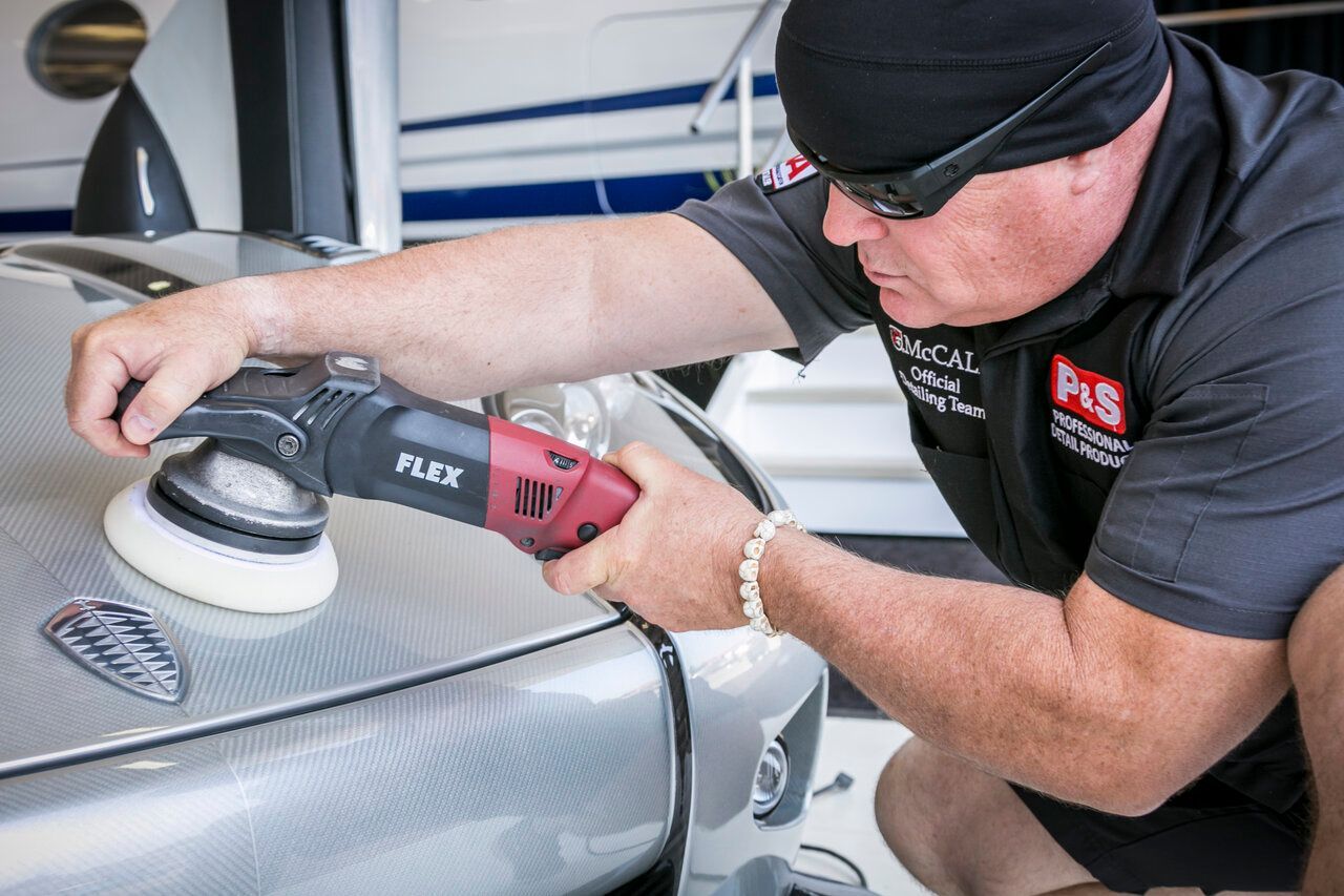 Man polishing silver car with a red and black electric buffer in a well-lit space.