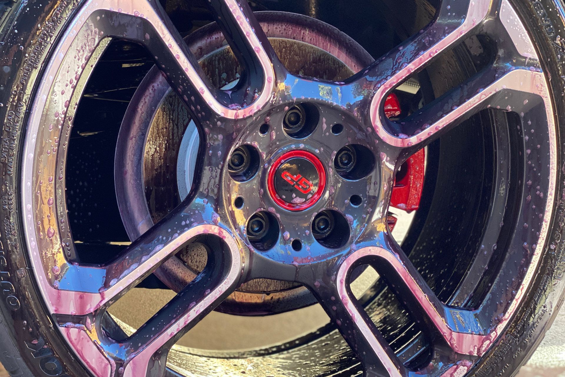 Close-up of a black car wheel with red accents, showing the hubcap and brake.