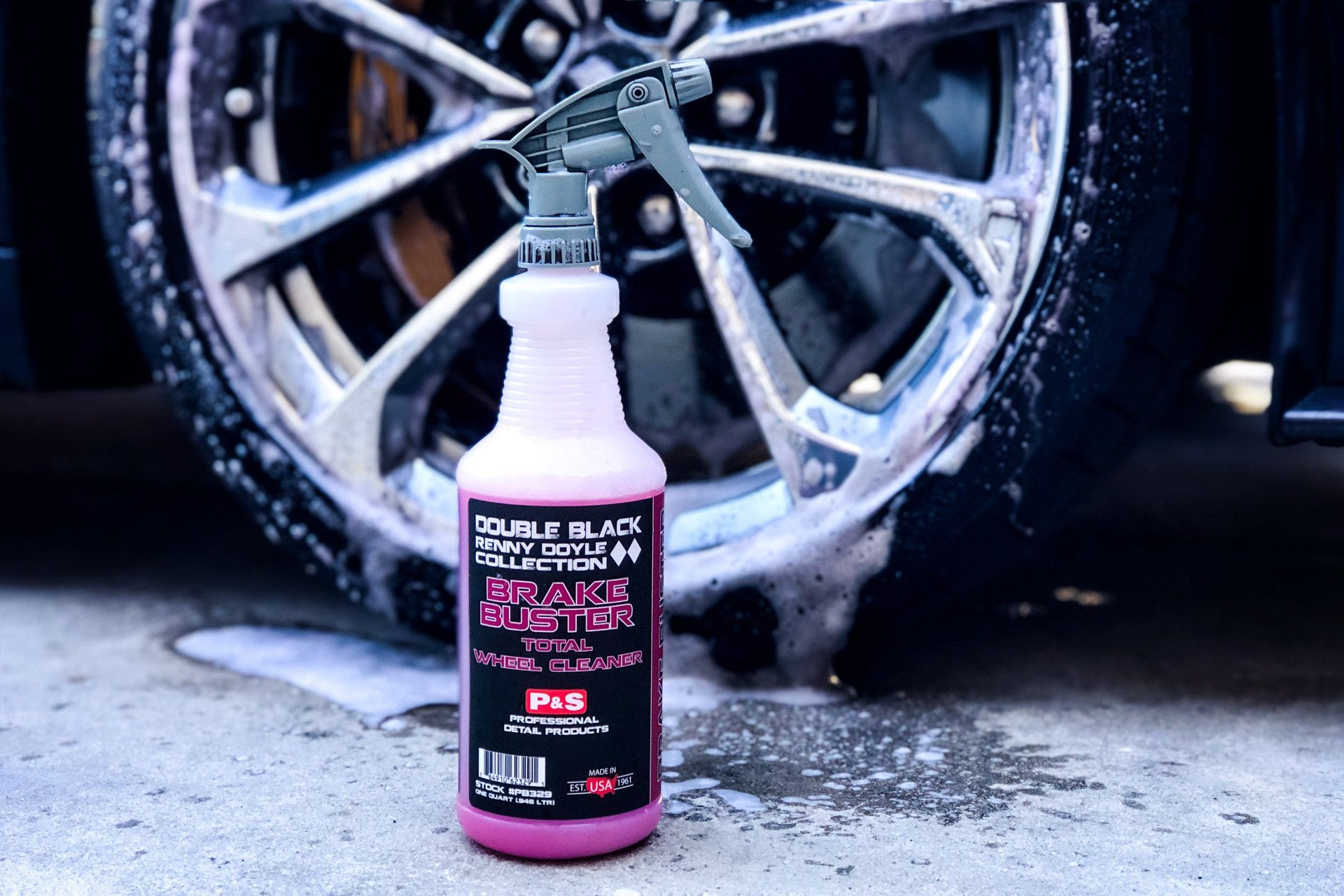 Pink spray bottle of car wheel cleaner in front of a car wheel with soapy foam.
