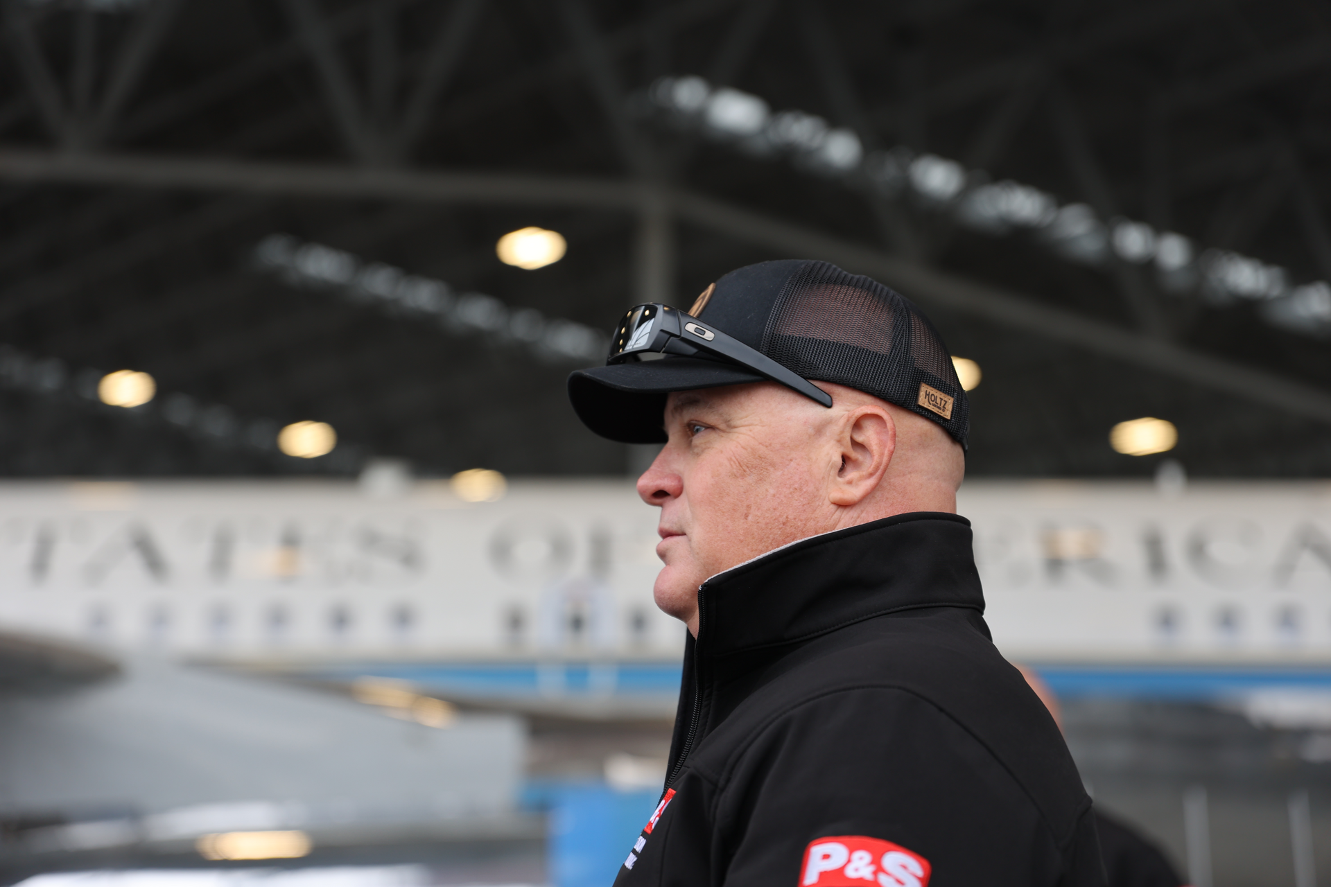 Man in black cap and jacket looks to the side near a building with
