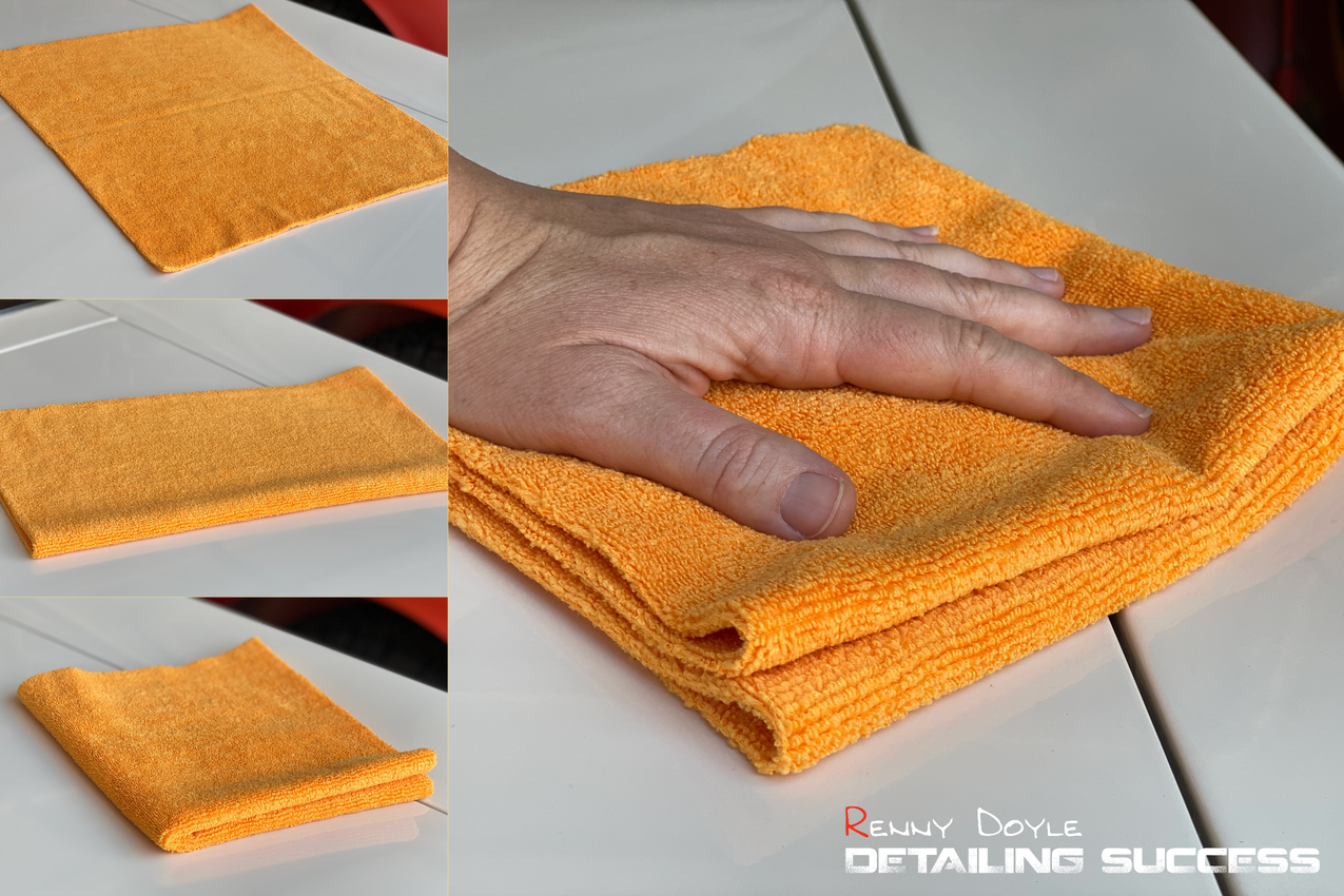 Orange microfiber cloth being used for detailing a white surface. Hand on cloth.