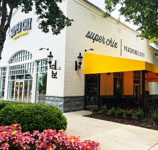 Super Chix restaurant in Peachtree City, white brick building, yellow awning, green shrubbery, and pink flowers.