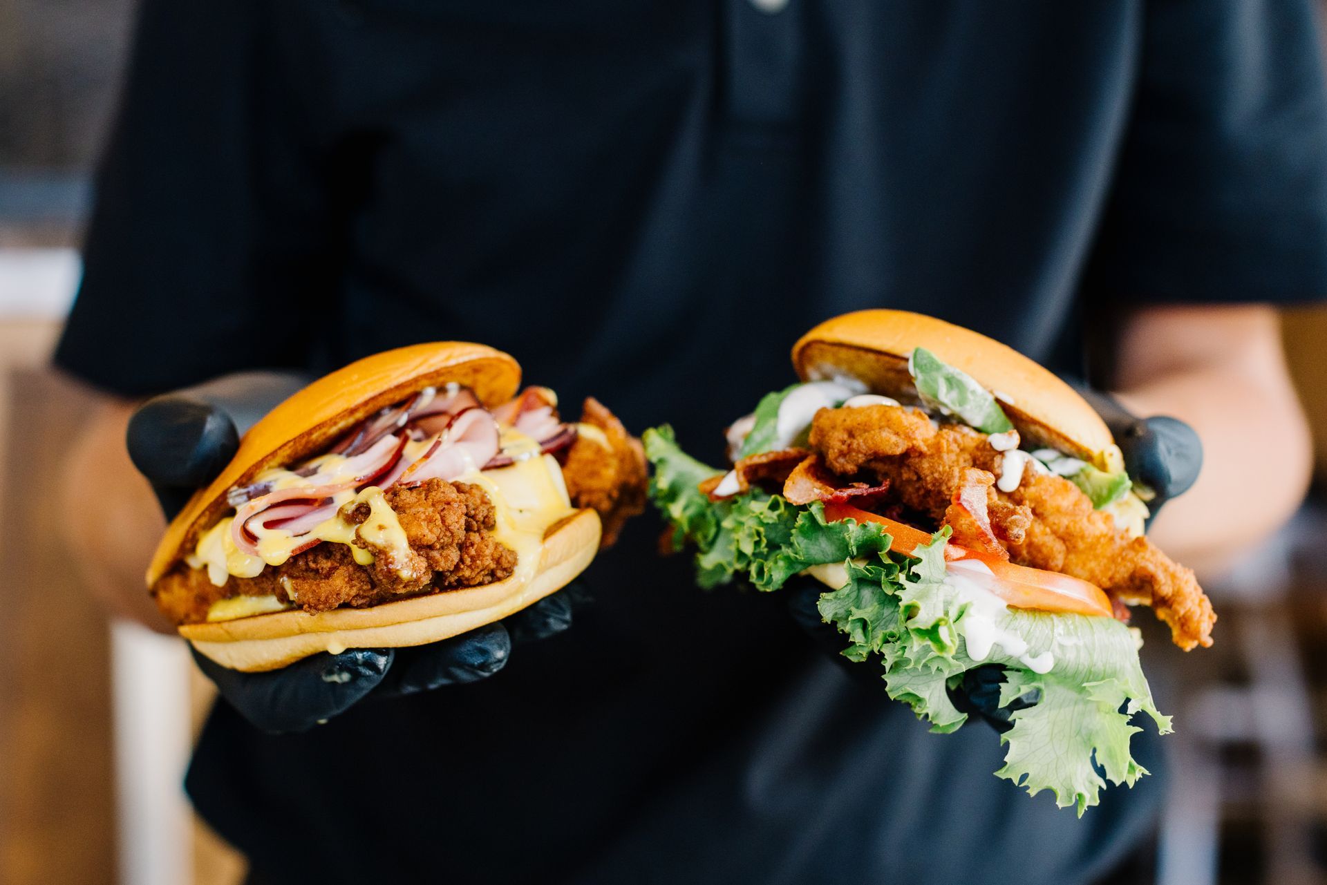 Person holding two fried chicken sandwiches, one with toppings and one with lettuce.