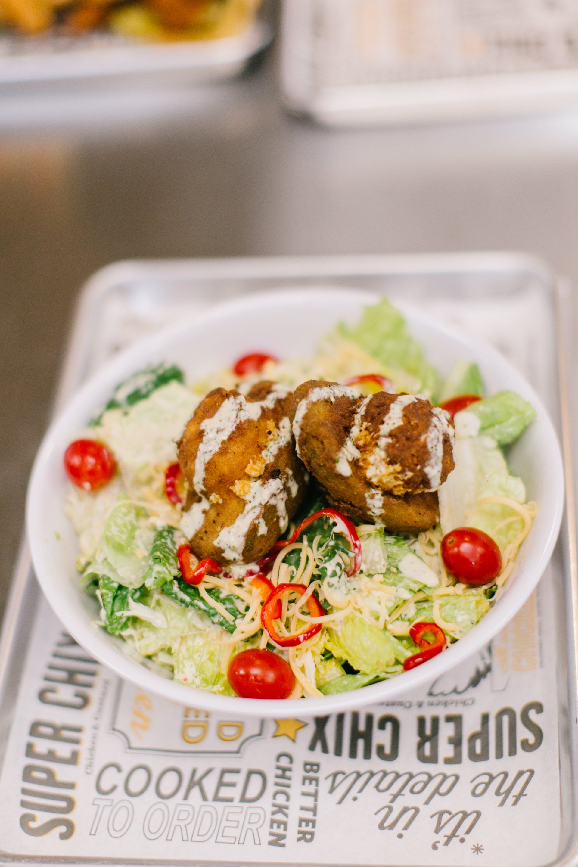 Falafel and cherry tomato salad with dressing, in a white bowl on a tray.