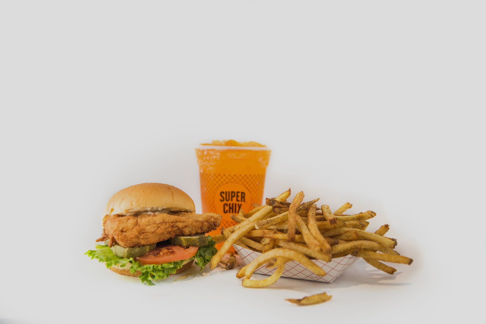 Chicken sandwich, fries, and orange drink on white background.