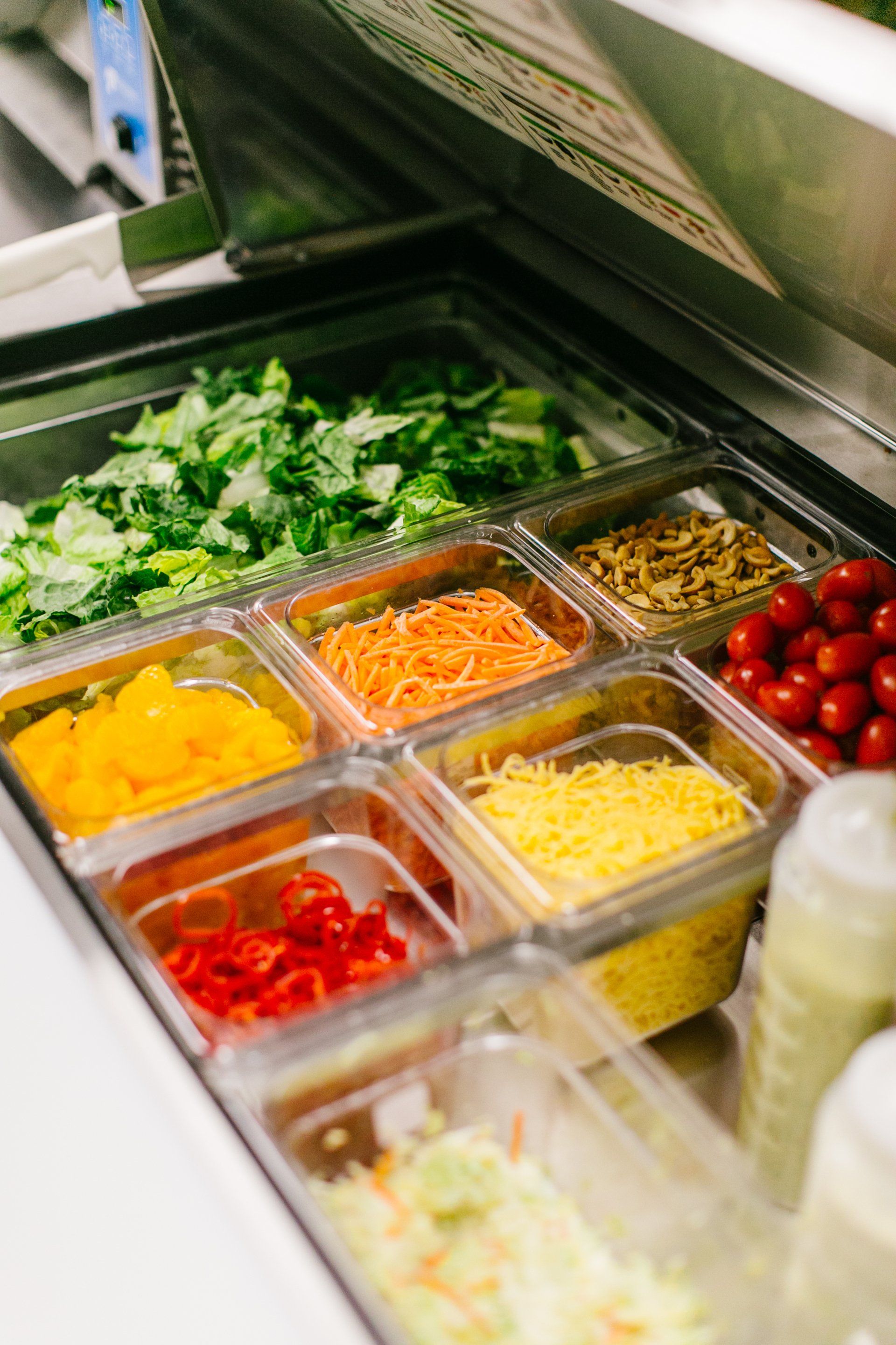 Salad bar with compartments of chopped lettuce, vegetables, and toppings.