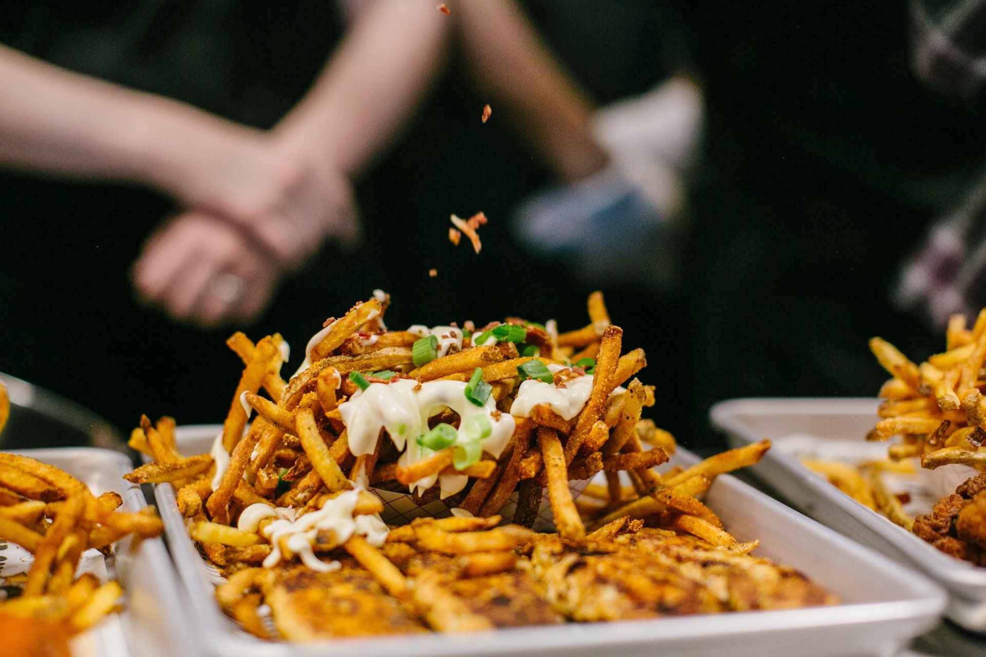 Tray of loaded fries with toppings; two people in the background.