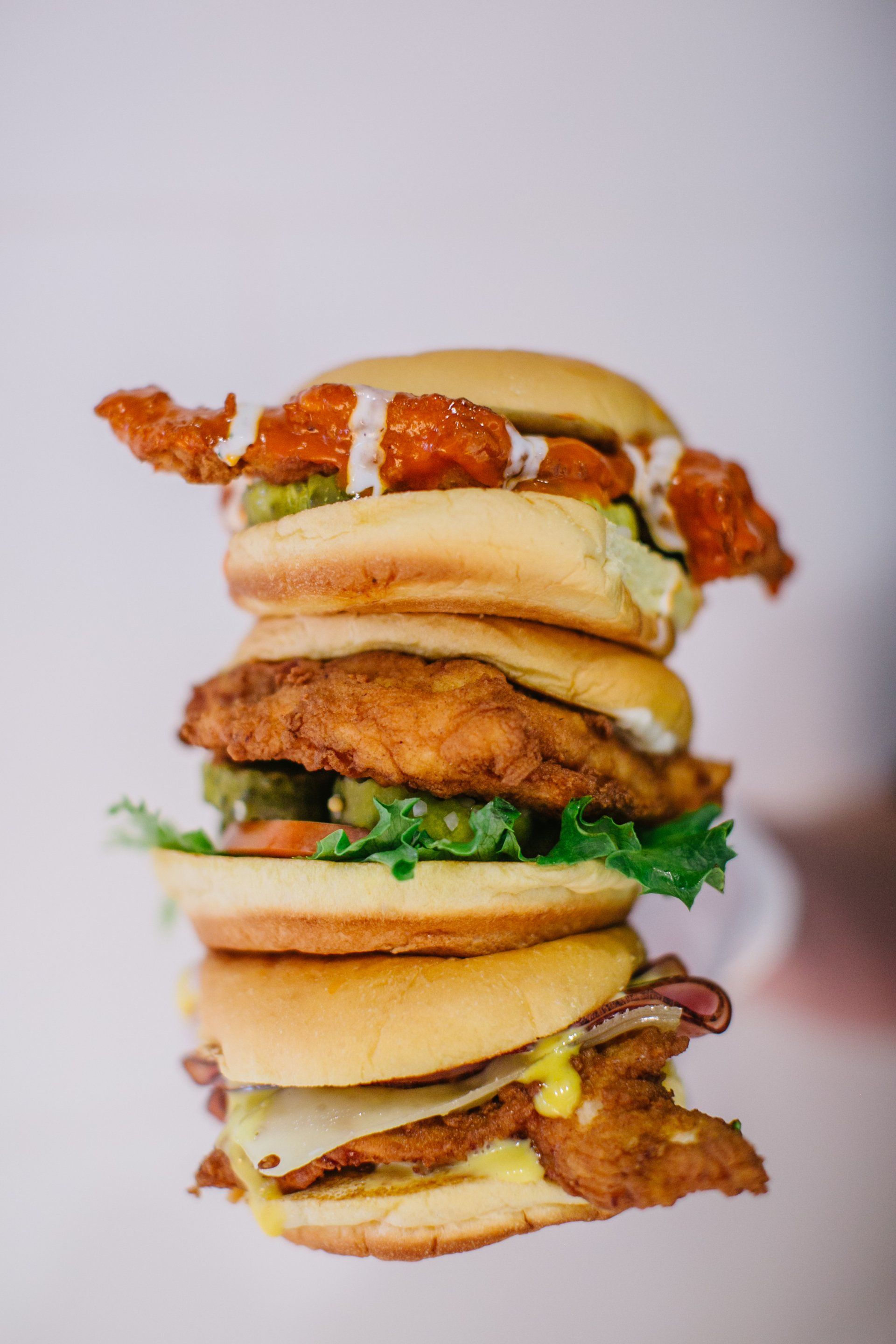 Stacked chicken sandwiches with varying toppings on white background.