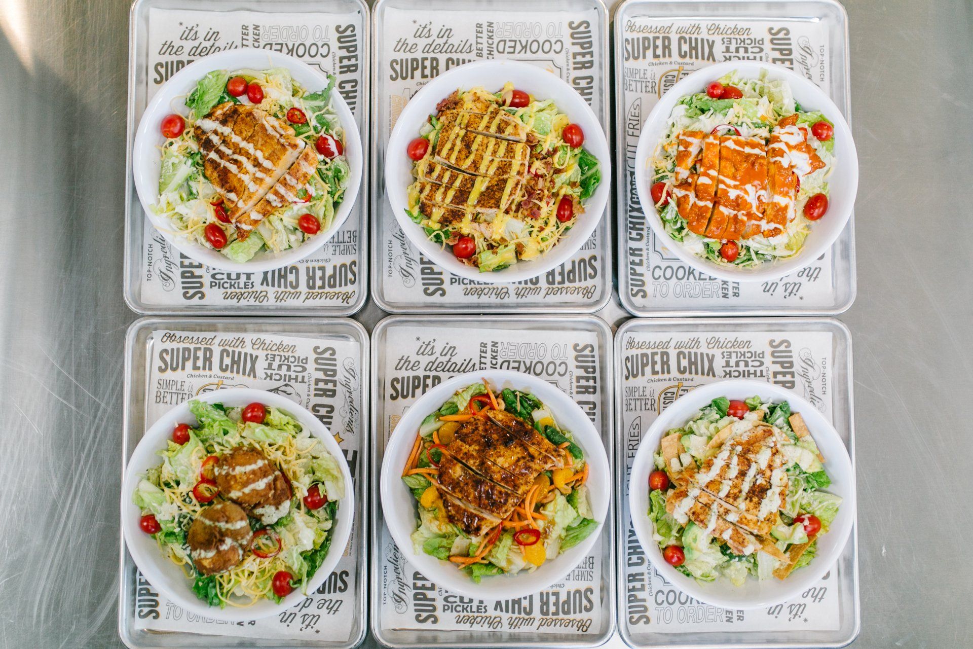 Six salads in white bowls on metallic trays, various toppings and dressings.