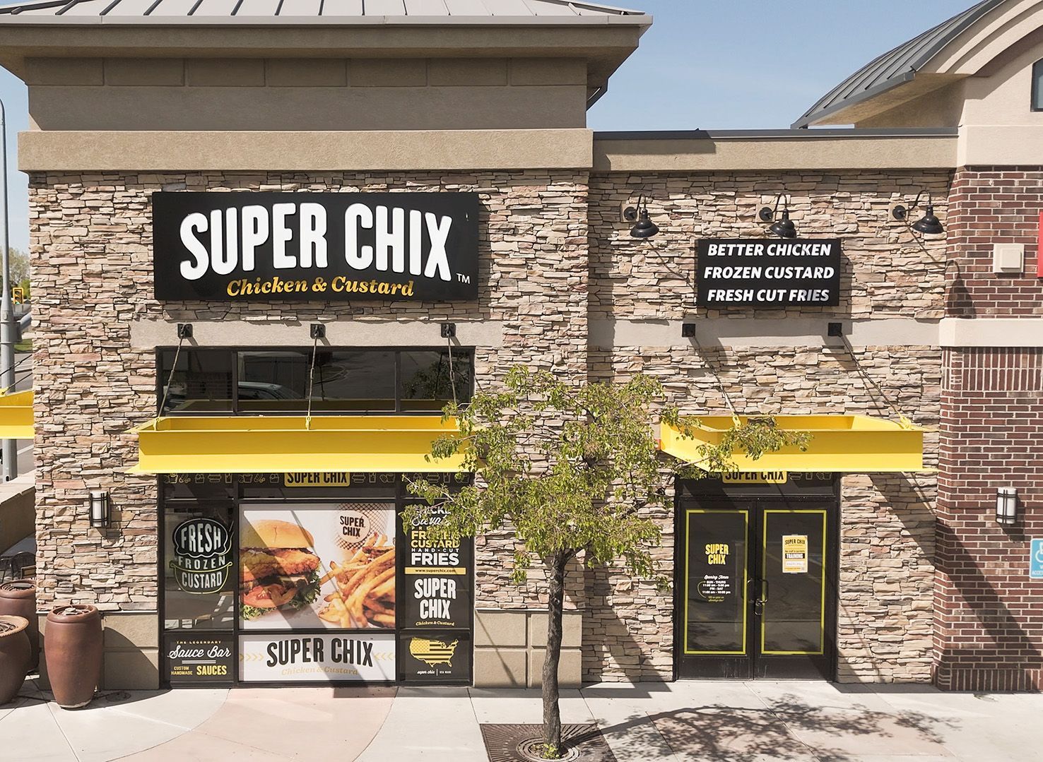 Super Chix restaurant exterior with stone and brick facade, yellow awnings, and sign.