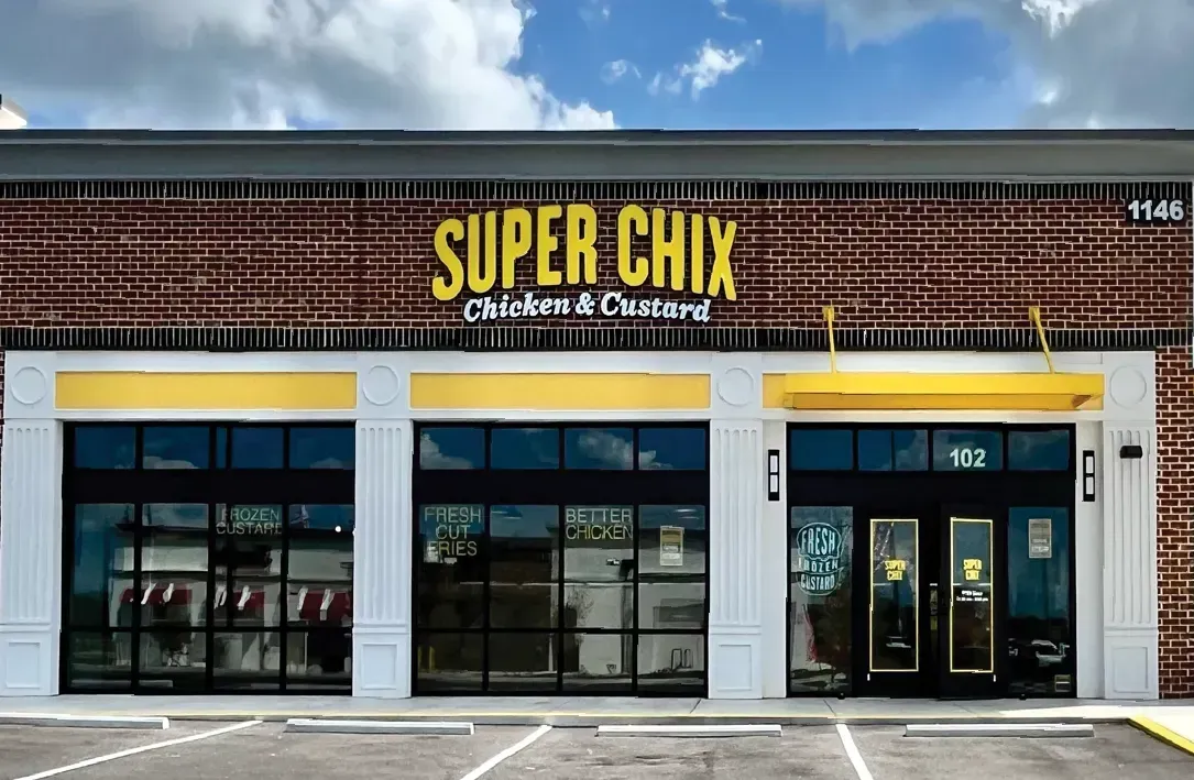Exterior view of a Super Chix restaurant with brick facade and yellow and black signage under a blue sky.