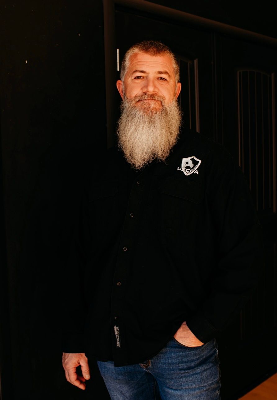 A man with a beard is wearing a black shirt and jeans.