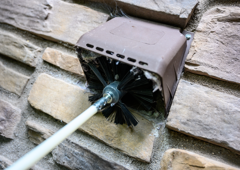 A brush is being used to clean a chimney on a brick wall.