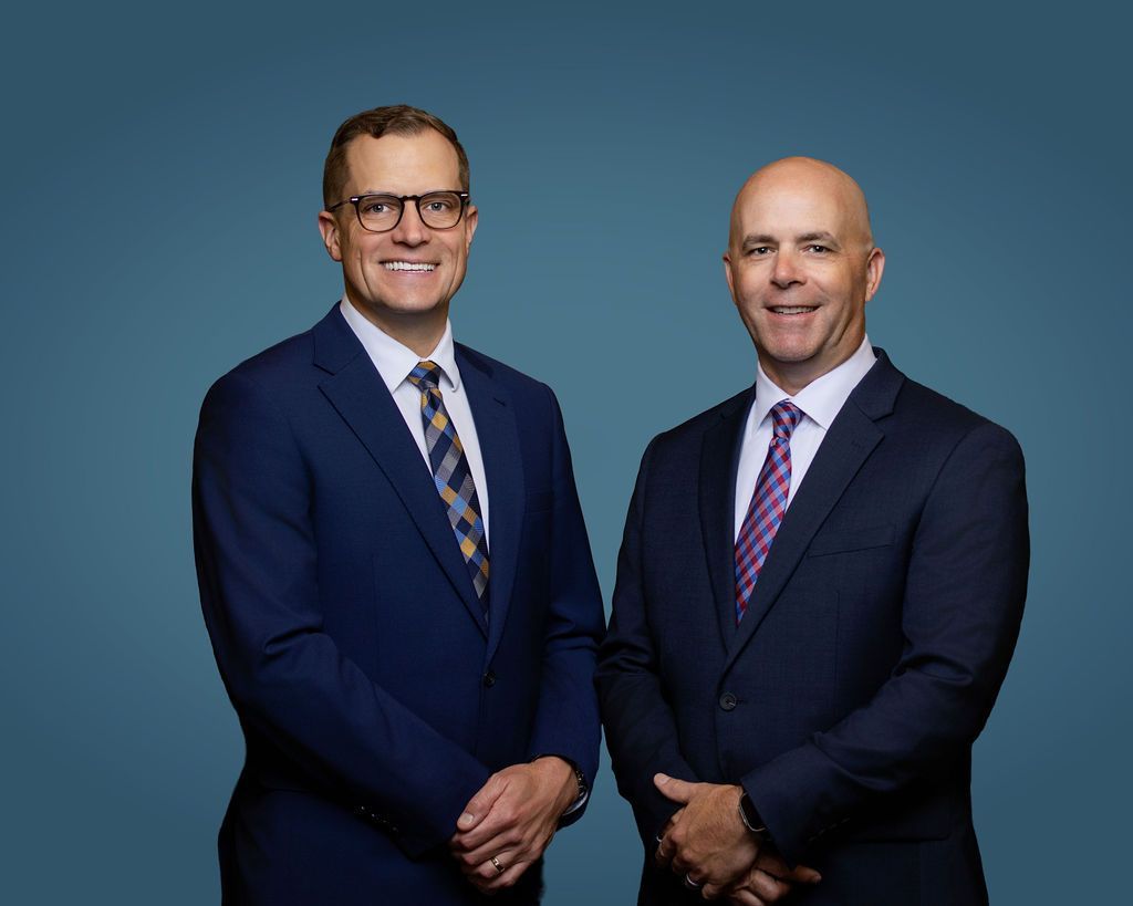 Two men in suits standing side by side against a blue studio background