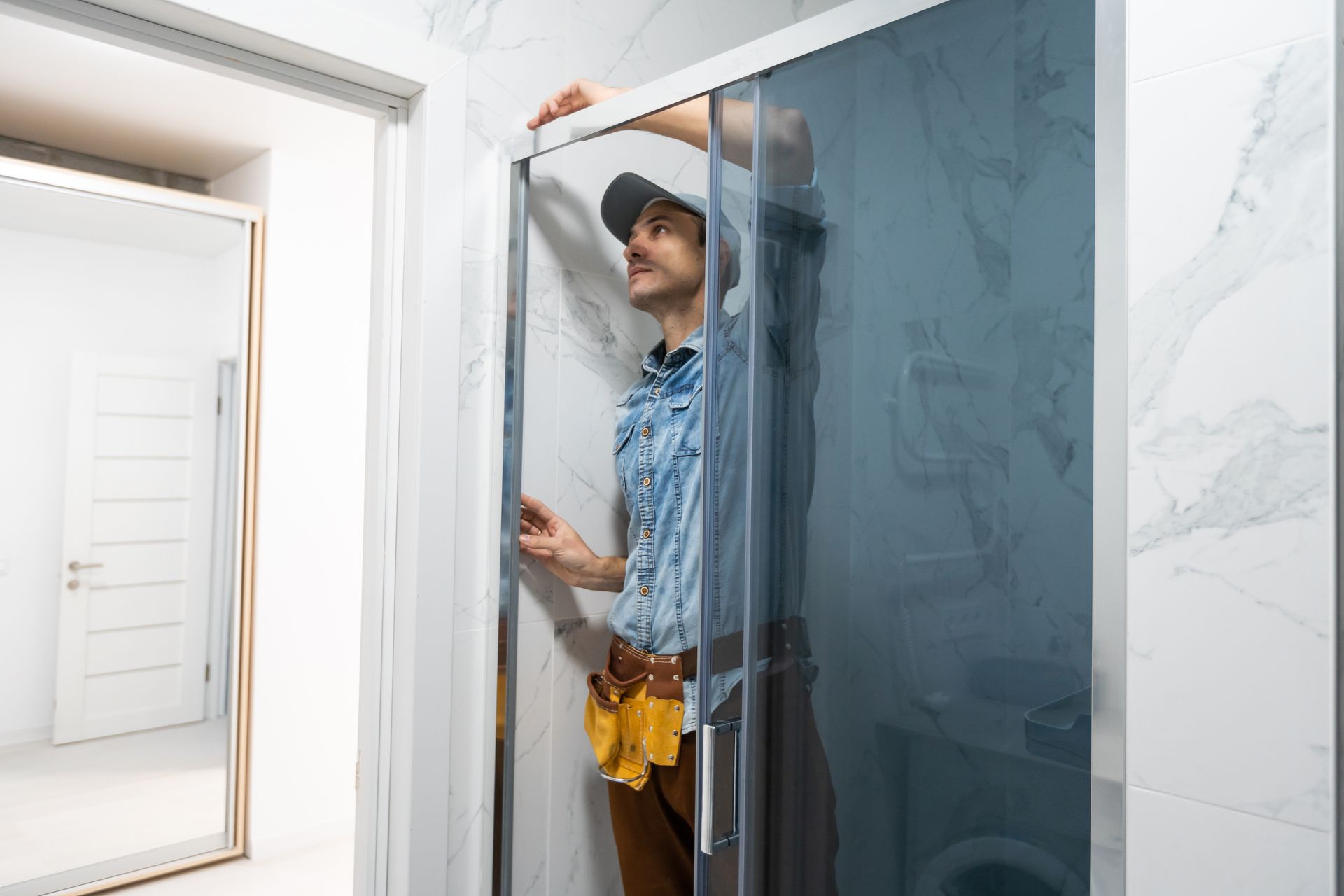 A technician repairing a sliding glass shower door in a bright tiled bathroom