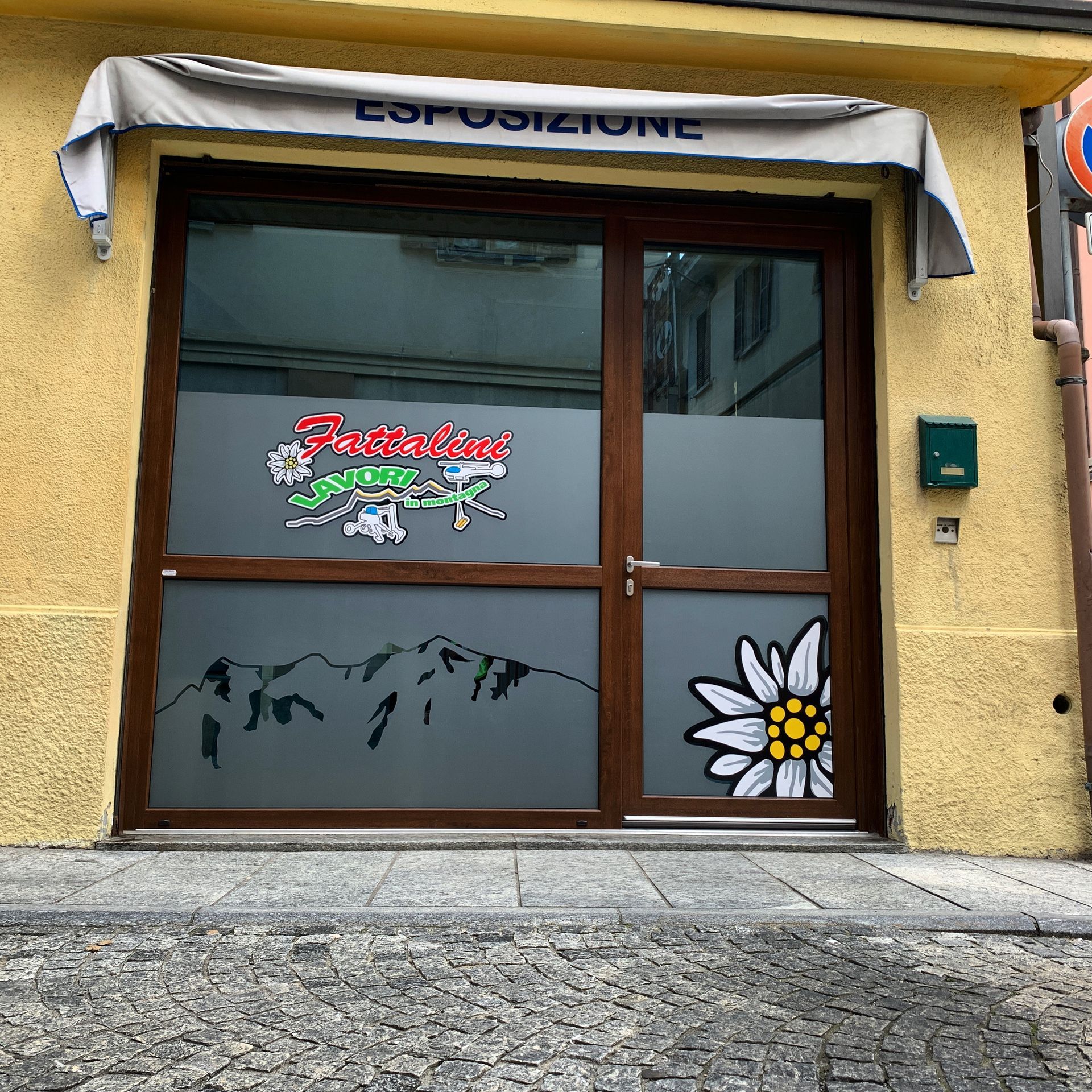 Vetrina con porta marrone, finestre smerigliate con l'immagine di una montagna e un grande fiore, e facciata gialla.