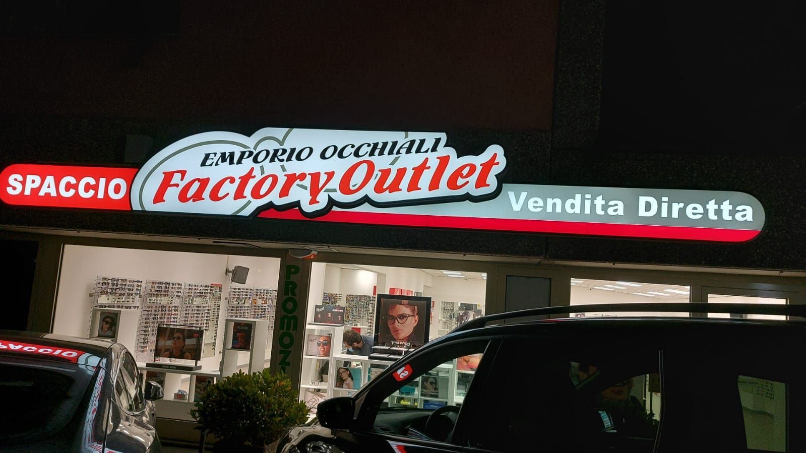 Veduta notturna di un negozio outlet di occhiali con un'insegna luminosa che riporta la scritta 