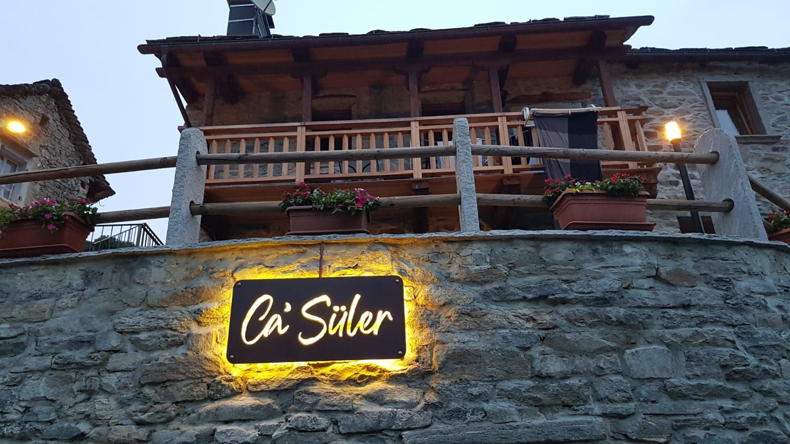 Un edificio in pietra con un balcone in legno e un'insegna luminosa con la scritta 