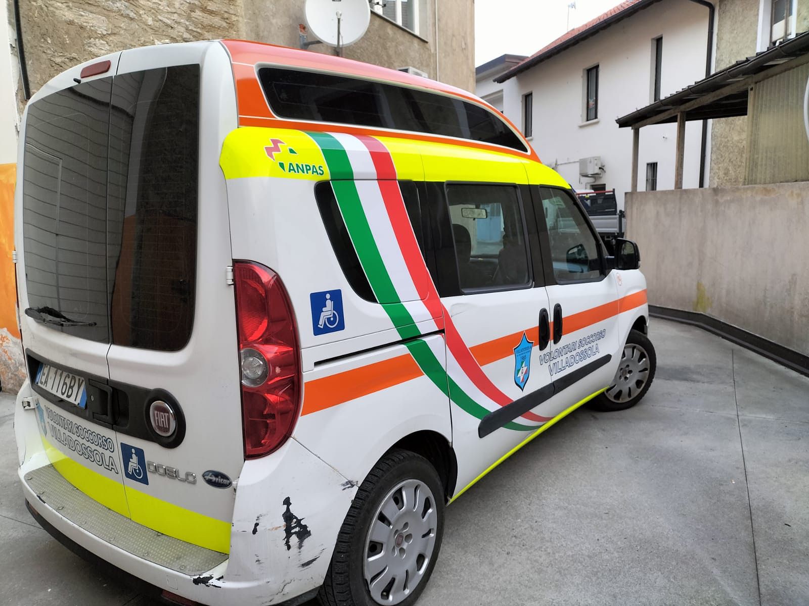 Furgone Fiat Doblò bianco, accessibile alle sedie a rotelle e decorato con strisce della bandiera italiana, parcheggiato all'aperto su una superficie pavimentata.