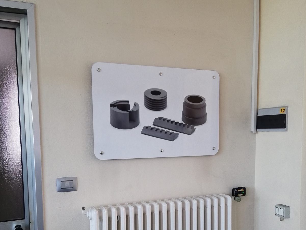 Un cartello a parete che mostra vari componenti di macchinari industriali, montato sopra un termosifone bianco in una stanza ben illuminata.