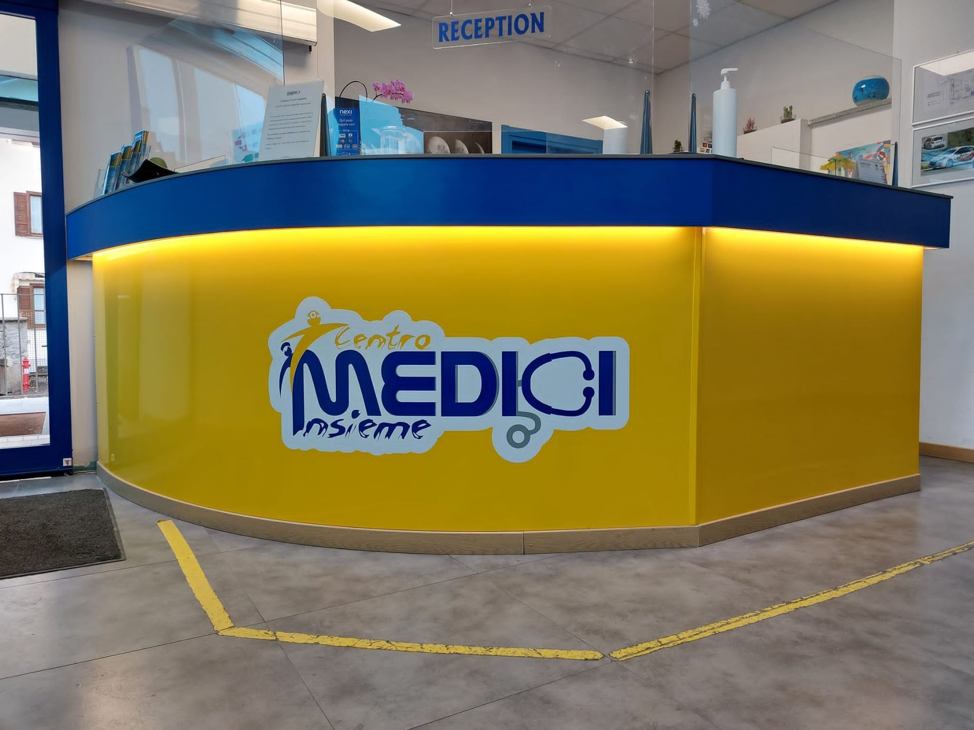 Un bancone reception curvo di colore giallo con il logo blu 