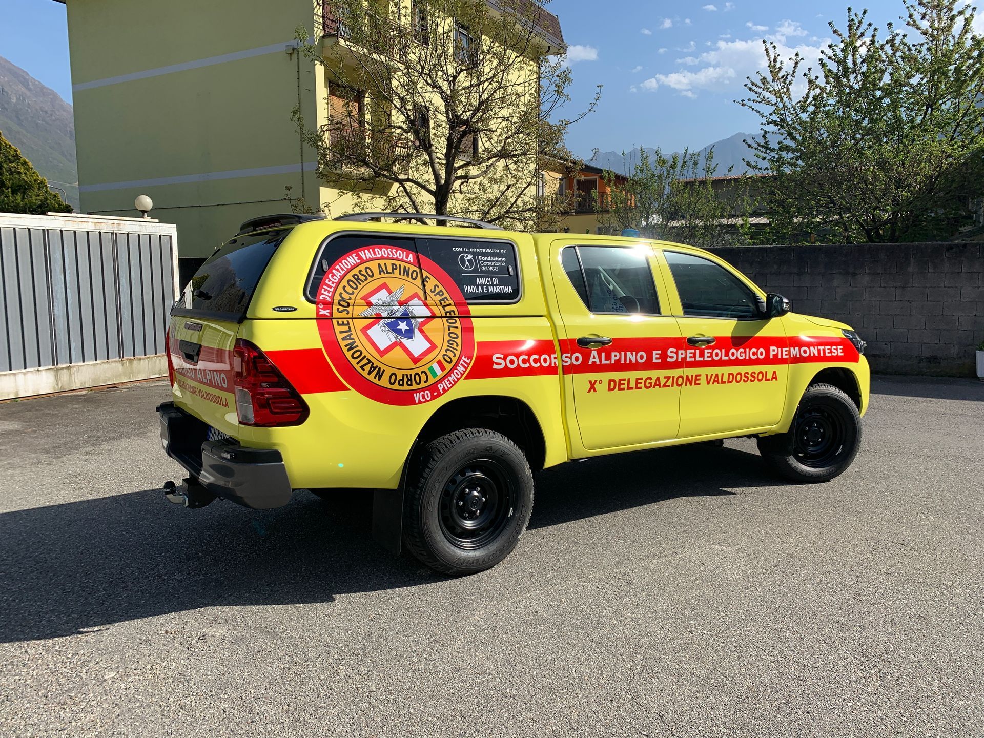 Un pick-up giallo del soccorso alpino parcheggiato su un piazzale ghiaioso di fronte a un edificio.