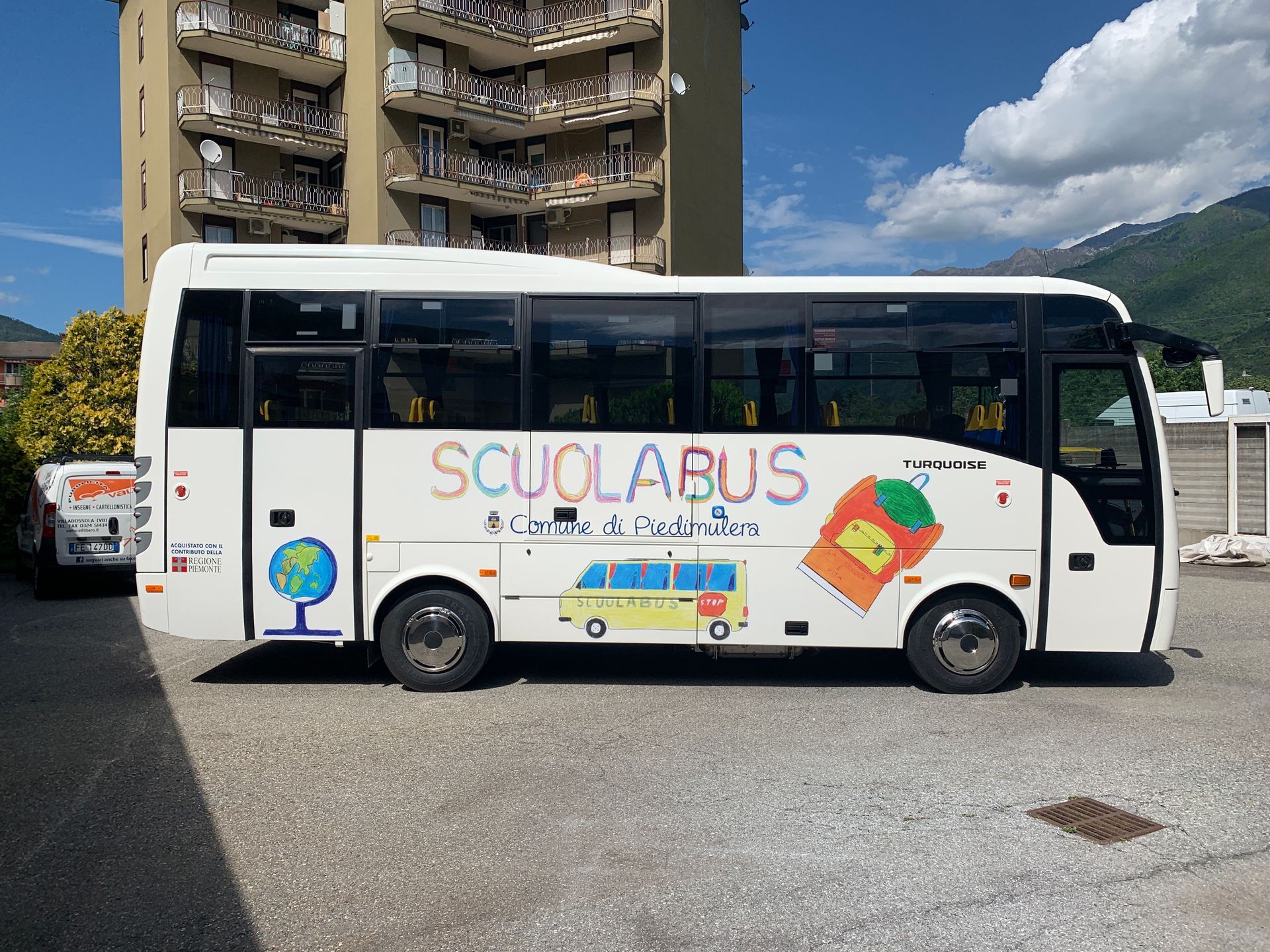 Uno scuolabus bianco parcheggiato all'aperto, decorato con grafiche colorate raffiguranti un mappamondo, un autobus più piccolo e uno zaino.
