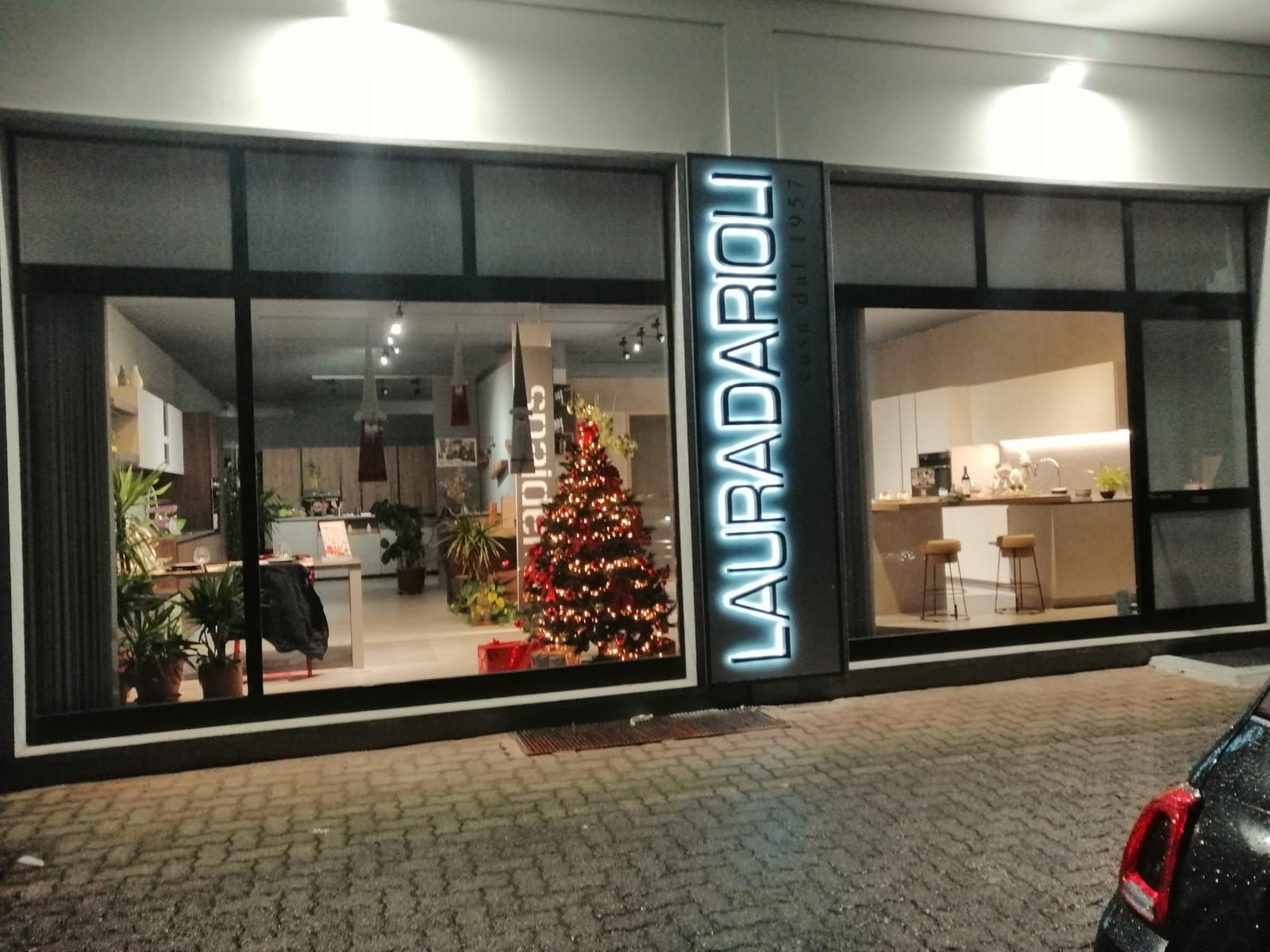 La vetrina notturna di Lauradaroli, con in mostra uno showroom di mobili da cucina e un albero di Natale decorato.