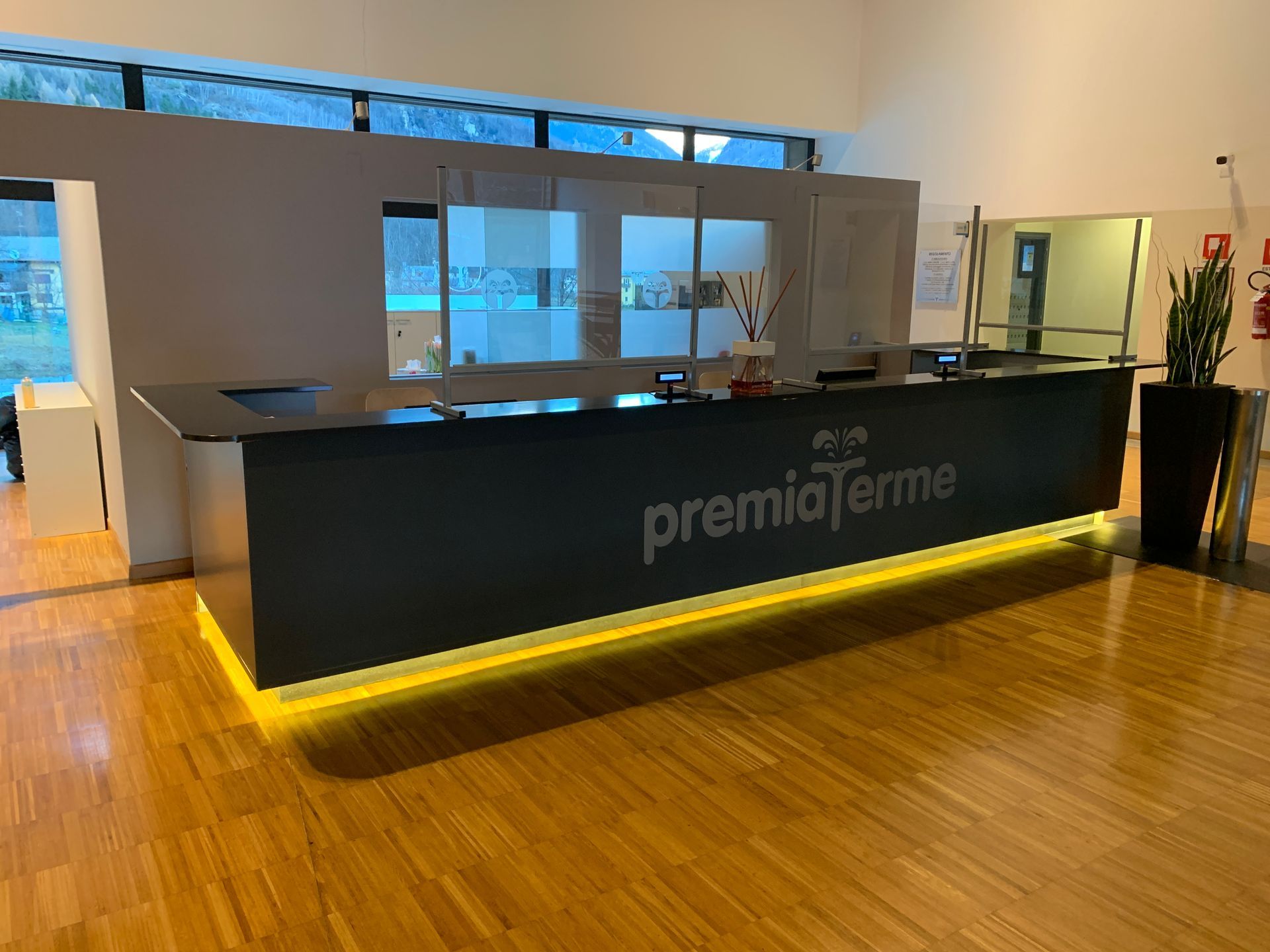 In una hall luminosa e moderna, illuminata da luci dorate, un bancone reception nero con il logo 