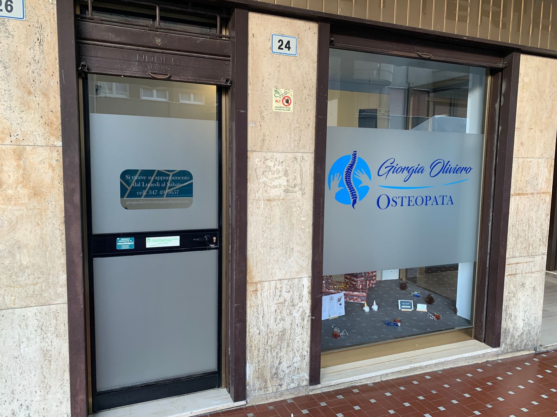 Ingresso dello studio dell'osteopata Giorgio Obinu con porta e finestra in vetro al numero 24 di un edificio rivestito in pietra.