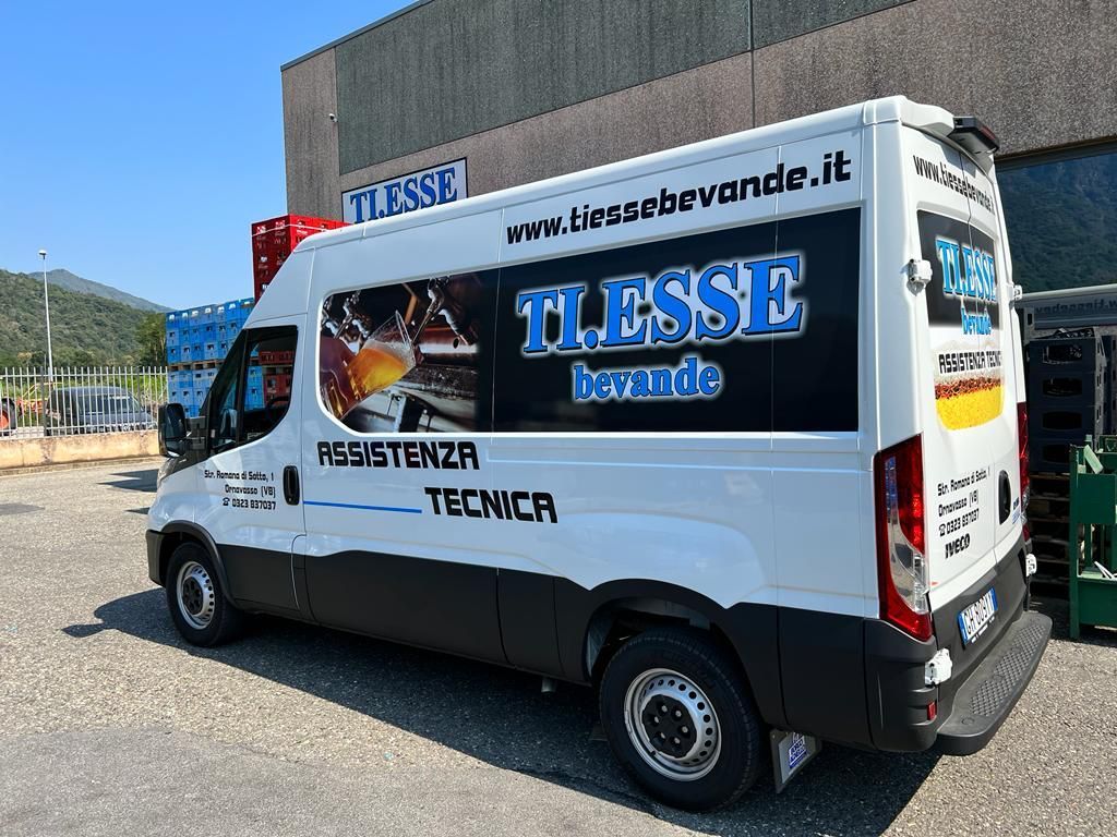 Un furgone bianco della TI.ESSE adibito alla vendita di bevande, parcheggiato in un piazzale ghiaioso in una giornata di sole.