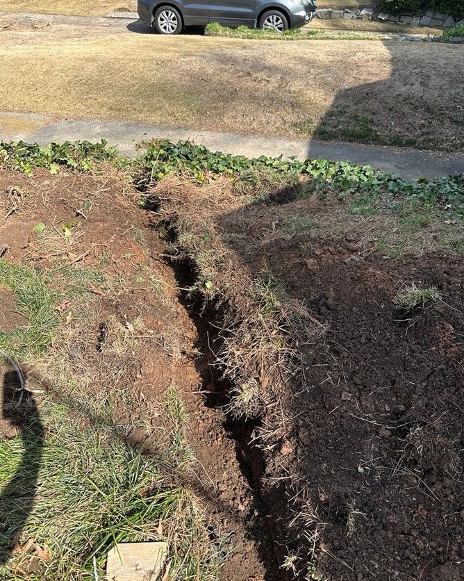 A man is kneeling down in the dirt next to a pipe.