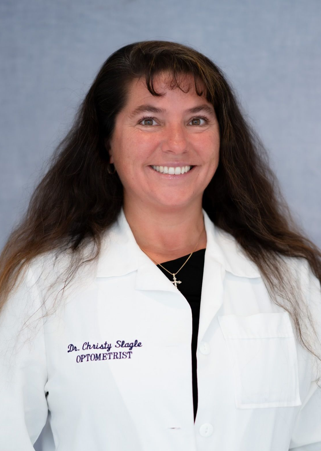 Portrait of an optometrist in a white coat, smiling against a gray background.