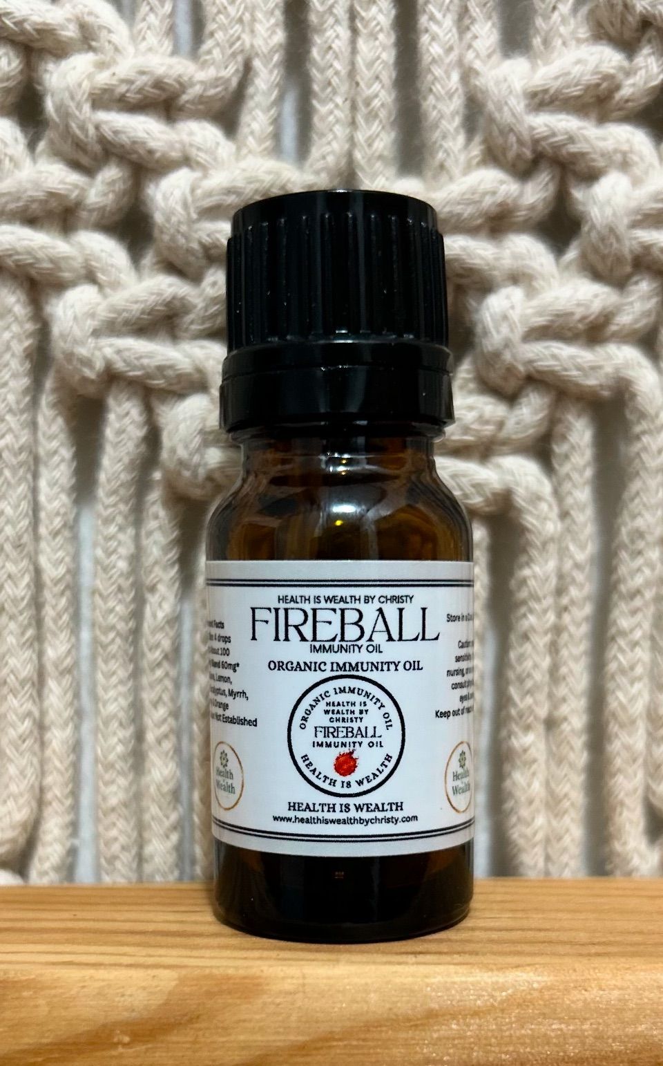 Small amber bottle labeled “Fireball” with a black cap, sitting on a wooden surface against a knit background