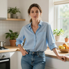 Person in a blue shirt and jeans standing in a bright kitchen near a fruit bowl.