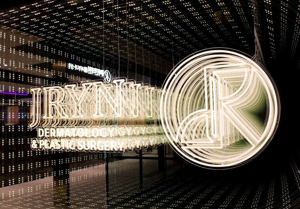 Illuminated JRYNNE? sign and circular R logo in a mirrored, gold-lit interior lobby