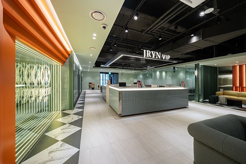 Modern hotel lobby with front desk, green wall, warm orange lighting, and seating area