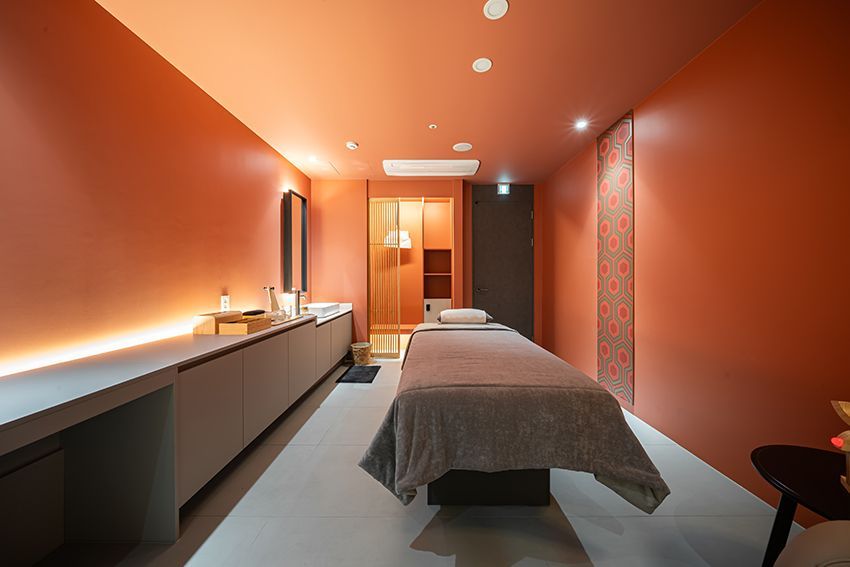 Modern spa treatment room with orange walls, two massage beds, and soft ambient lighting