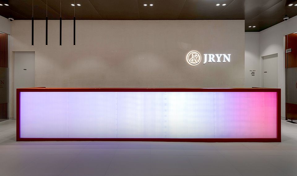 Modern lobby with a long glowing pink-white reception desk and JRYN logo on the wall
