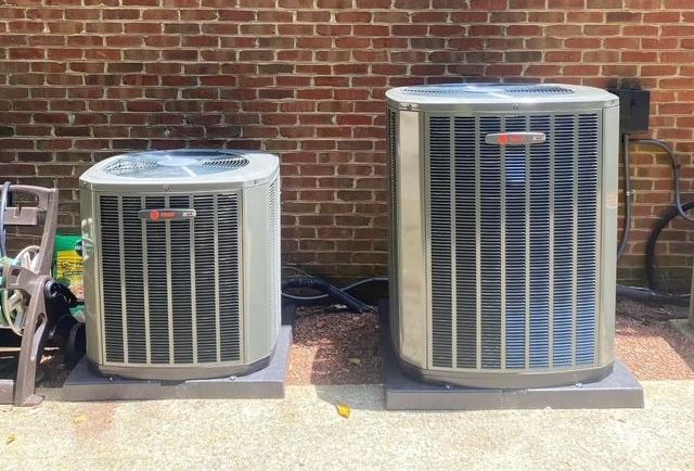 Two air conditioners repaired by John's Heating, Cooling, and Appliance Repair are sitting next to each other in front of a brick wall in Peachtree City