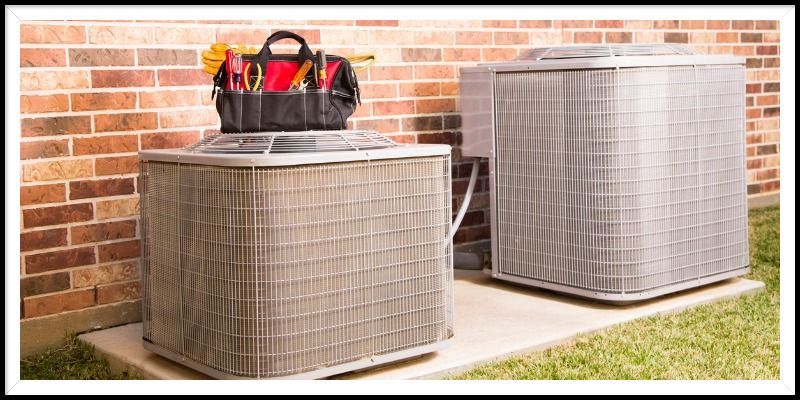 Two air conditioners are sitting next to each other on the side of a brick building.