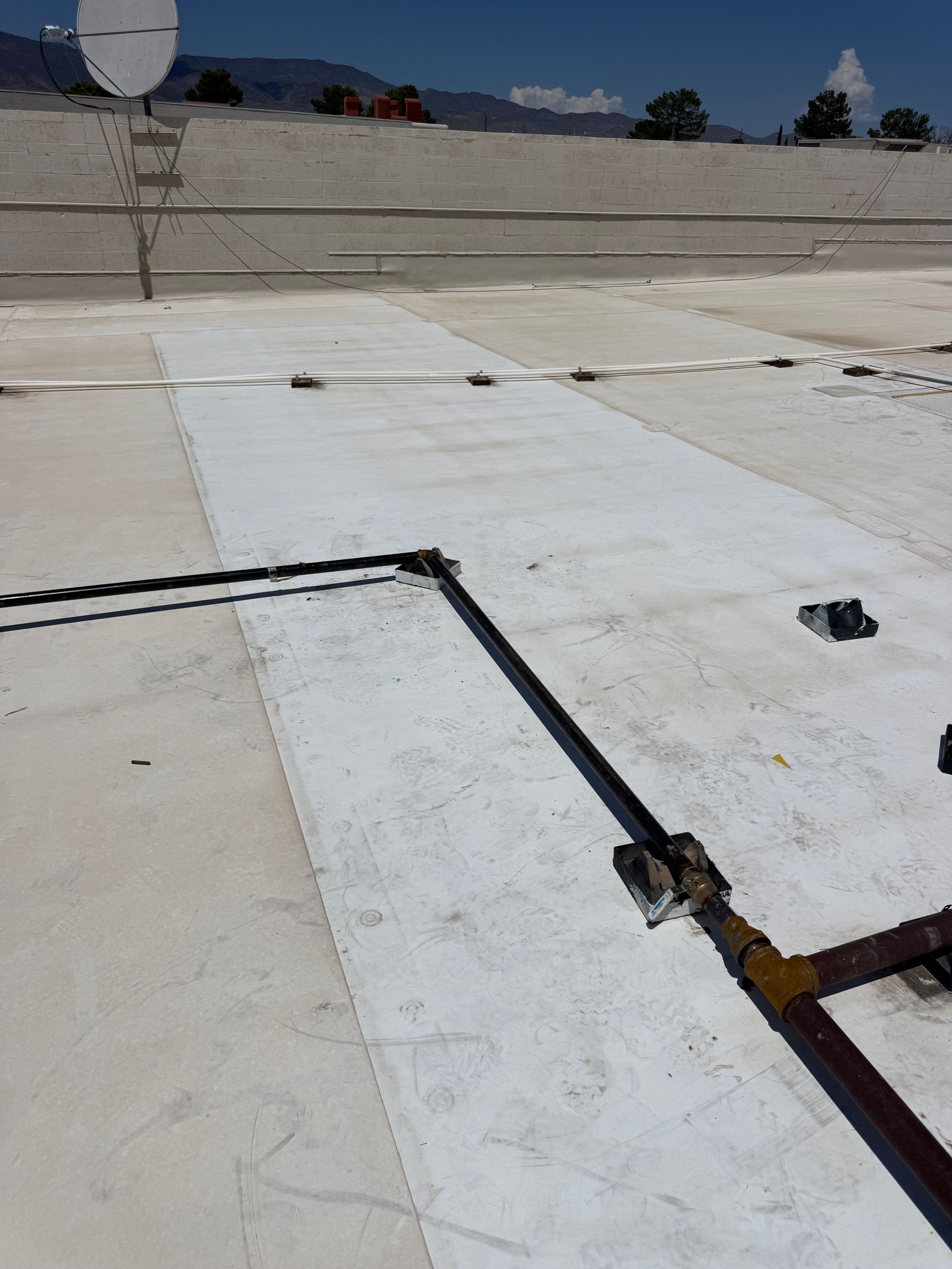 Flat rooftop with white waterproof membrane, drainage pipe, and satellite dish under a blue sky