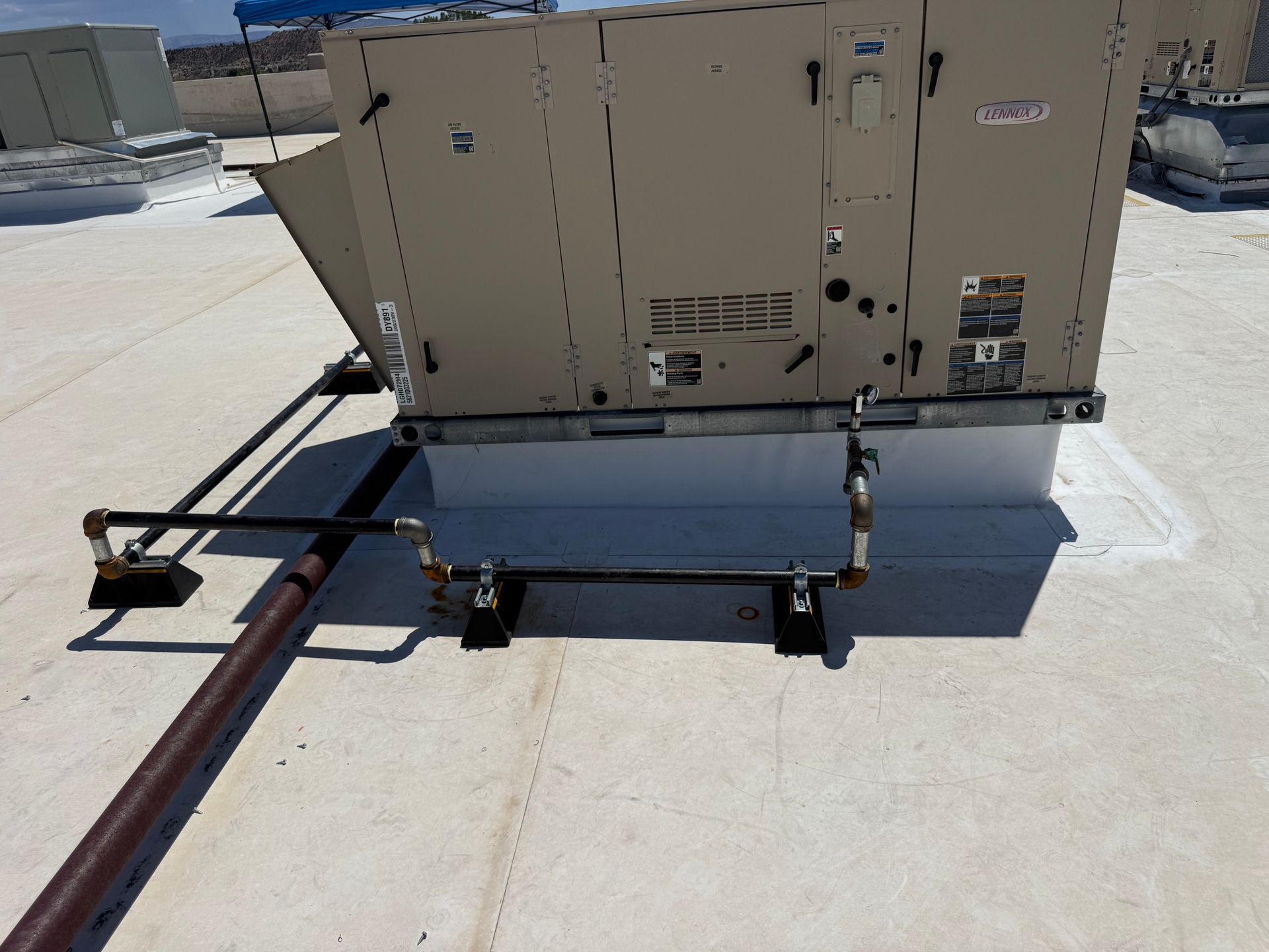 Beige HVAC unit mounted on rooftop rails with pipes and cables nearby