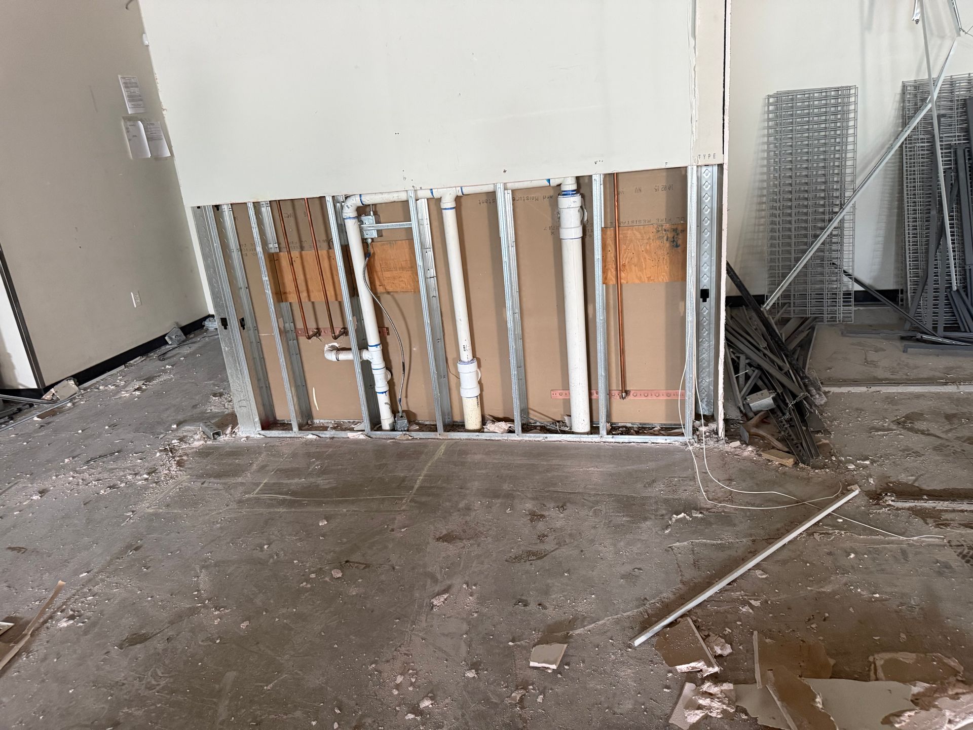 Damaged interior wall with exposed studs, debris on the floor, and a wet patch in an unfinished room.